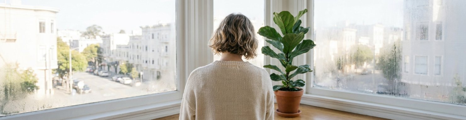 Personne de dos devant une fenêtre embuée regardant une rue qui semble lointaine, image de l'effet de vitre de la déréalisation